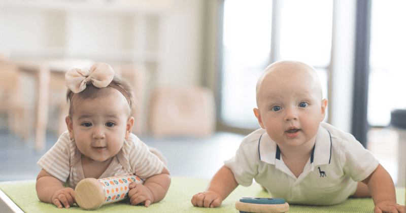 A smiling infant lying on their tummy on a soft mat in a bright, modern infant care environment, engaging in tummy-time play.