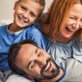 Family life is about fun. young smiling family of four having fun while lying on bed and hugging each other