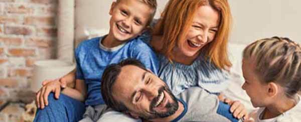 Family life is about fun. young smiling family of four having fun while lying on bed and hugging each other